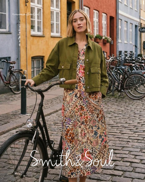 Eine Frau in einem rosa Hemd und einer Strickjacke mit weißer Hose posiert vor einem weißen Hintergrund. Der Text lautet "Smith & Soul" am unteren Rand.