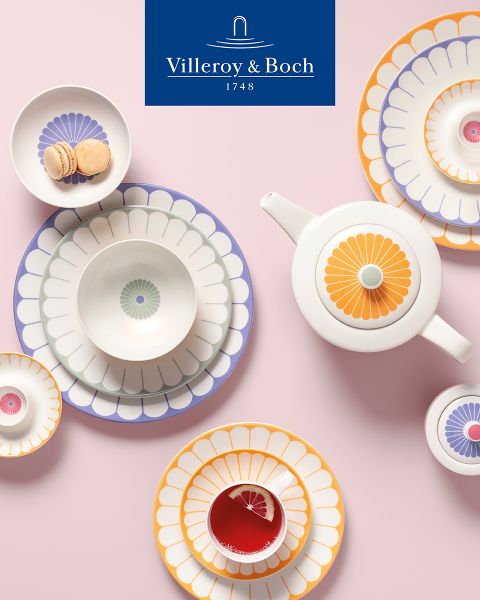 Eine Küchenausstellung zeigt eine schwarze Schüssel mit kleinen Schneebesen auf einem rechteckigen Tablett. Daneben steht eine Platte mit Glasdeckel, auf der Käse und frische Kräuter liegen. Oben prangt das Logo von Villeroy & Boch.
