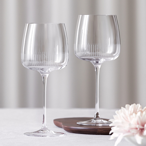 Ein stilvolles Arrangement aus drei eleganten Cocktailgläsern auf einem dunklen Tisch mit einer Keramikvase, in der belaubte Zweige hängen. Jedes Glas enthält ein klares Getränk und Garnituren. Die Szene ist warm beleuchtet und hat einen goldenen Hintergrund.