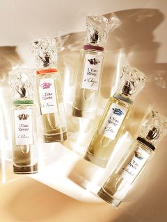 Fünf Flakons des Parfüms „Sisley L’Eau Rêvée“ sind auf einer weißen Fläche mit Lichtreflexen angeordnet; jeder Flakon hat ein Etikett und einen Verschluss in einer anderen Farbe.