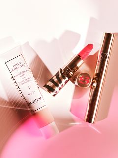 Sisley-Kosmetikprodukte, darunter eine getönte Feuchtigkeitscreme, ein rosa Lippenstift in einer Hülle mit Zebramuster und eine goldene Mascara-Tube, angeordnet vor einem hellen Hintergrund.