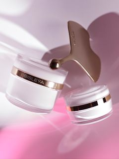 Zwei Tiegel mit Sisleÿa-Hautpflegecreme und ein goldenes Gesichtsmassagegerät, die vor einem zartrosa-weißen Hintergrund schweben.