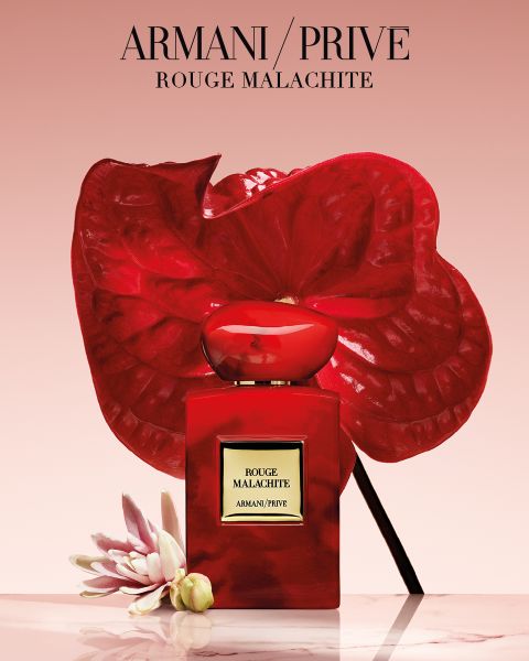 Ein roter Parfümflakon von Armani/Privé „Rouge Malachite“ mit tropischen Blumen vor einem rosa Hintergrund mit Farbverlauf.