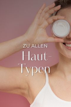 Eine lächelnde Person in einem weißen Tanktop hält sich vor einem rosa Hintergrund einen Cremetiegel vors Auge. Der Text auf dem Bild lautet „Zu allen Haut-Typen.“.
