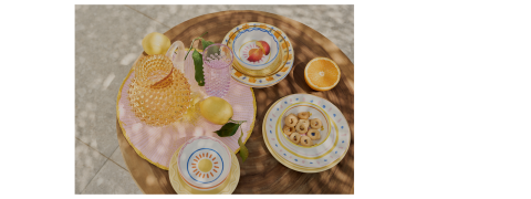 Ein runder Holztisch mit bunten Tellern, einer Schüssel Kekse, halbierten Orangen, Zitronen und strukturiertem Glasgeschirr, alles auf einem rosa gestreiften Tischtuch im natürlichen Sonnenlicht arrangiert.