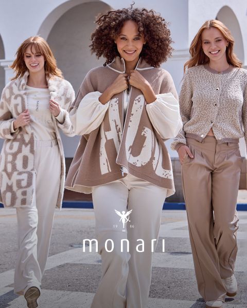 Drei Frauen tragen stilvolle Monari-Outfits in neutralen Tönen, darunter beige und cremefarbene Pullover, Jacken und weite Hosen. Das Monari-Logo und die Aufschrift „1986“ sind unten im Bild zu sehen.