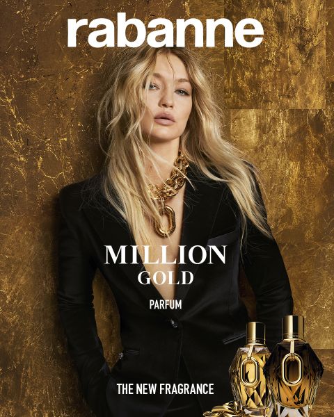 Ein Modell in einem schwarzen Anzug mit langem, gewelltem blondem Haar trägt eine klobige goldene Halskette und steht vor einem Hintergrund mit goldener Struktur. Oben steht "rabanne", unten stehen "MILLION GOLD PARFUM" und zwei goldene Parfümflaschen.
