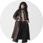 Eine Frau mit lockigem Haar trägt einen langen braunen Mantel, einen cremefarbenen Pullover, eine dunkle Hose mit weitem Bein und einen gemusterten Schal. Sie hält eine Clutchbag und steht vor einem schlichten weißen Hintergrund.