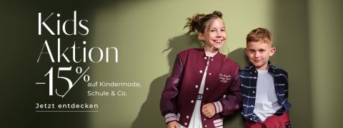 Zwei lächelnde Kinder posieren vor einer grünen Wand; das Mädchen trägt eine bordeauxfarbene Uniformjacke, der Junge ein kariertes Hemd. Deutscher Text wirbt für "Kids Aktion -15% auf Kindermode, Schule & Co. Jetzt entdecken.