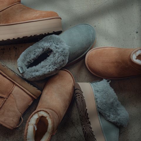 Mehrere Paar gemütliche, pelzgefütterte Winterstiefel aus Wildleder in hellbraunen und grauen Farben sind auf einem glatten, hellen Boden angeordnet. Die Sohlen sind dick und strukturiert, und die Stiefel werden von oben betrachtet.