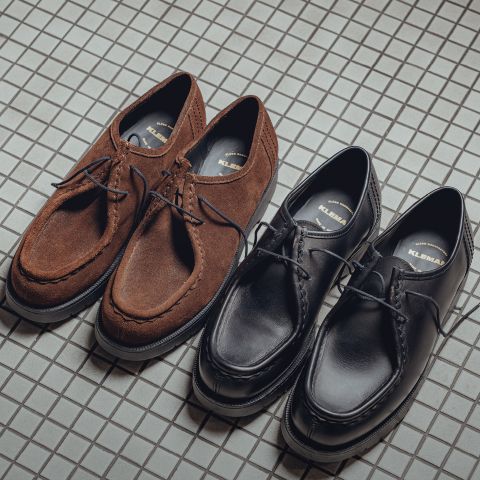 Zwei Paar Schnürschuhe auf einem gefliesten Boden: ein Paar aus braunem Wildleder und das andere aus schwarzem Leder, beide mit dicken Sohlen und einem lässigen, an Mokassins erinnernden Design.