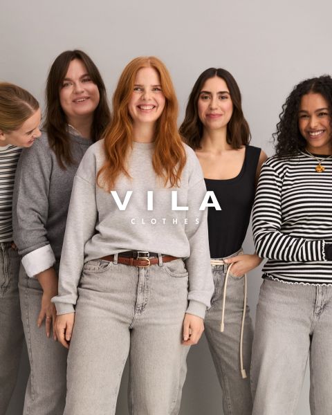 Fünf Frauen in Freizeitkleidung, darunter Jeans und Oberteile in neutralen Farben, stehen eng beieinander und lächeln vor einem schlichten Hintergrund. Der überlagerte Text lautet "Vila Clothes".
