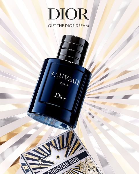 Ein Flakon des Parfums Dior Sauvage Elixir steht über einer dekorativen Dior-Schachtel, aus deren Hintergrund goldene, silberne und weiße Strahlen hervortreten. Der Text lautet: "Dior. Verschenken Sie den Dior Traum.