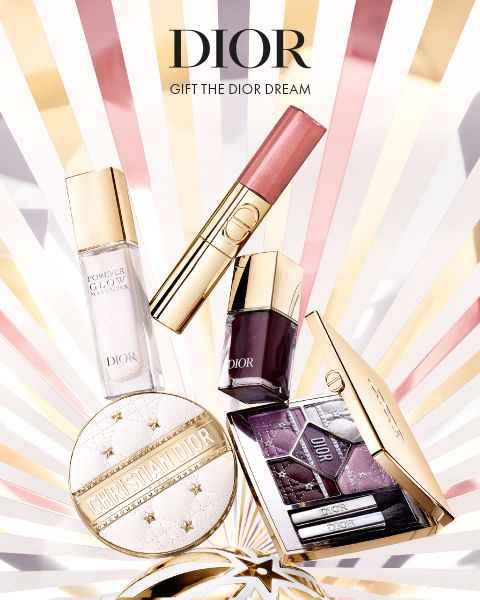 Eine Auslage mit Dior-Schönheitsprodukten, darunter Grundierung, Lippenstift, Nagellack, eine Puderdose und eine Lidschattenpalette, vor einem leuchtenden Hintergrund mit dem Text "DIOR Gift the Dior Dream" am oberen Rand.