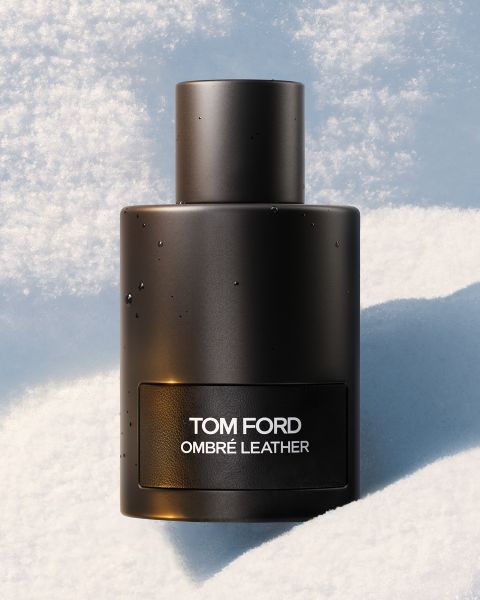 Ein schwarzer Flakon des Parfums Tom Ford Ombré Leather steht aufrecht auf einer weichen, verschneiten Oberfläche, auf der feine Wassertropfen sichtbar sind.