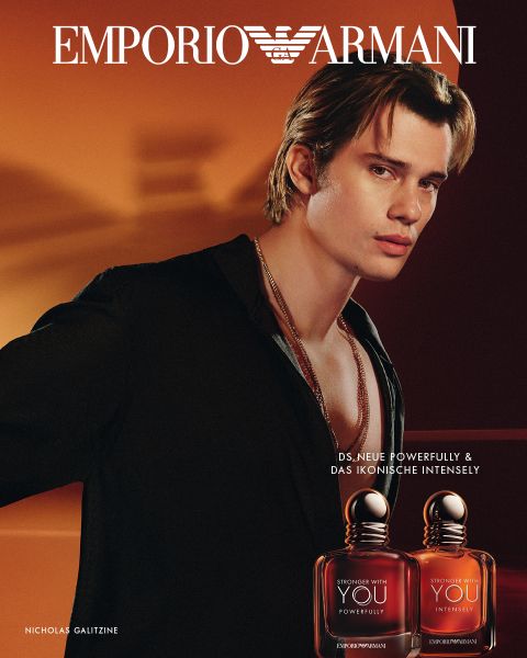 Ein junger Mann posiert vor Braun- und Orangetönen mit zwei Emporio Armani "Stronger With You"-Duftflaschen im Vordergrund.