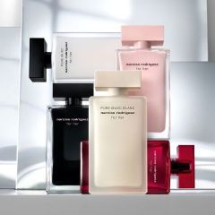 Fünf Parfümflakons von Narciso Rodriguez in Schwarz, Weiß, Rosa und Rot stehen aufrecht und sind vor einem spiegelnden, modernen Hintergrund gestapelt.