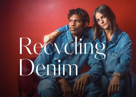 Zwei Personen in Jeansoutfits sitzen nebeneinander vor einer roten Wand; über das Bild ist der Schriftzug „Recycling Denim“ gelegt.