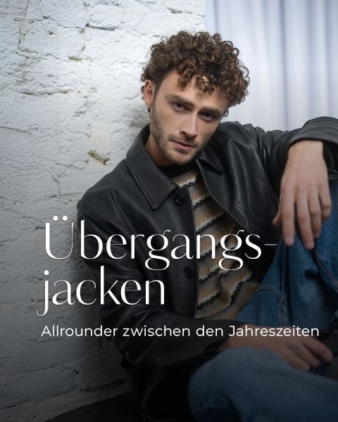 Ein Mann in Lederjacke und gestreiftem Pullover sitzt an einer weißen Backsteinmauer. Der Text lautet: "Übergangsjacken - Allrounder zwischen den Jahreszeiten.