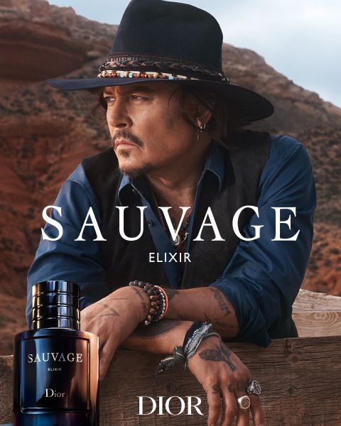 Ein Mann mit Hut und Weste lehnt an einem Holzgeländer in der Wüste, im Vordergrund ein Flakon des Parfums Sauvage Elixir Dior mit Logo.