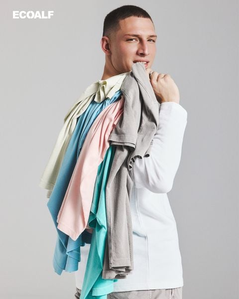 Eine Person in einem weißen Hemd lächelt, während sie mehrere bunte T-Shirts über der Schulter trägt. Das Wort "ECOALF" steht in der oberen linken Ecke.