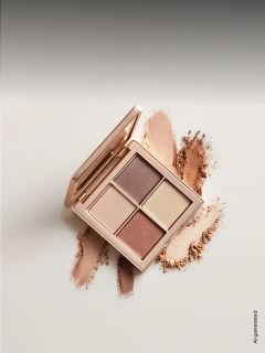 Eine offene Lidschattenpalette mit vier neutralen Farbtönen, umgeben von Swatches der Puder auf einer hellen Fläche.