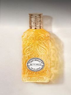 Verschnörkelter Glasflakon mit goldener Flüssigkeit, geprägtem Muster und silbernem Etikett mit der Aufschrift "Patchouly TRD Eau de Parfum".