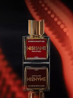 Ein Flakon des Parfums "Hundred Silent Ways" von Nishane mit einer goldenen Kappe, die sich unten spiegelt, und einem verschwommenen roten und schwarzen Hintergrund.