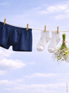 Marineblaue Boxershorts, weiße Socken und ein kleiner Blumenstrauß, der an einer Wäscheleine vor einem blauen Himmel mit Wolken hängt.