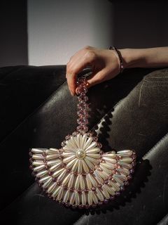 Eine Hand hält eine perlenbesetzte Handtasche mit Perlen- und rosa Blumenmustern, die auf einer schwarzen, strukturierten Lederoberfläche ruht.