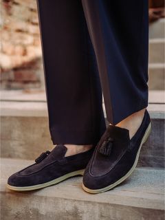 Eine Person, die dunkle Wildlederschuhe mit hellen Sohlen und eine dunkle Hose trägt, steht auf einer Außentreppe.