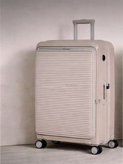 Beigefarbener Hartschalenkoffer mit horizontalen Rillen, aufrecht stehend auf vier Rädern, mit ausgezogenem Teleskopgriff.