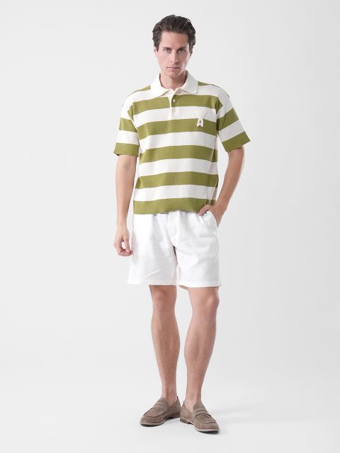 Mann in grün-weiß gestreiftem Poloshirt, weißen Shorts und braunen Halbschuhen vor einem schlichten weißen Hintergrund.