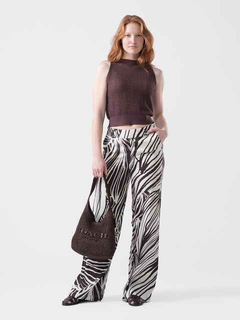 Eine Frau trägt ein ärmelloses braunes Oberteil, eine weit geschnittene Hose mit Zebramuster, schwarze Sandalen und eine braune Coach-Tasche.