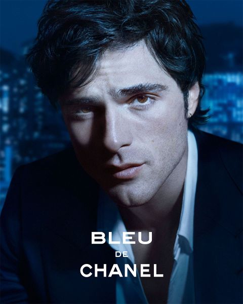 Ein Mann in einem dunklen Anzug blickt aufmerksam in die Kamera, während die Lichter der Stadt im Hintergrund verschwimmen; der Text lautet "Bleu de Chanel".