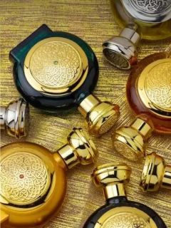 Fünf kunstvoll verzierte Parfümflakons mit aufwendig gearbeiteten goldenen Verschlüssen und Verzierungen, angeordnet vor einem schimmernden, goldfarbenen Hintergrund mit Struktur.