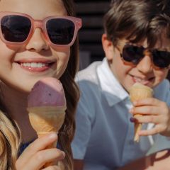 Zwei lächelnde Kinder mit Sonnenbrillen genießen an einem sonnigen Tag Eiswaffeln im Freien.