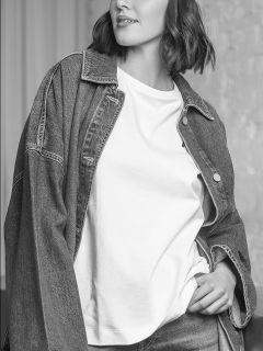 Eine Frau in Jeansjacke und weißem T-Shirt, die mit einer Hand in der Hosentasche posiert; das Bild ist in Schwarz-Weiß.