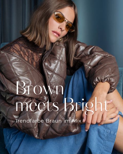 Eine Frau in einer braunen Steppjacke, einer blauen Hose und einer bernsteinfarbenen Sonnenbrille sitzt mit angezogenem Knie da; der Text lautet „Brown meets Bright“ und „Trendfarbe Braun im Mix“.