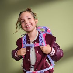 Ein lächelndes Mädchen in einer weinroten Jacke und mit einem bunten Rucksack steht vor einem schlichten hellgrünen Hintergrund.