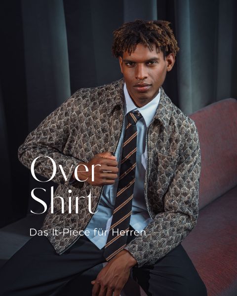Ein Mann in einem gemusterten Overshirt, Krawatte und Hemd sitzt auf einer roten Bank. Der Text lautet: „Overshirt – das It-Piece für Herren.“.