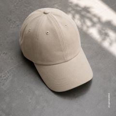 Auf einem grauen Fliesenboden liegt eine beige Baseballkappe, im Hintergrund sind Sonnenlicht und sanfte Schatten zu sehen.