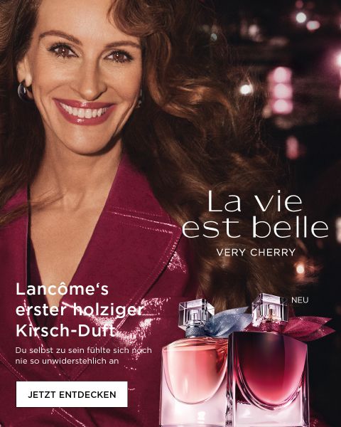 Eine lächelnde Frau in einem rosa Outfit steht hinter zwei Flaschen Lancôme-Parfüm; auf dem Bild ist der Text „La vie est belle VERY CHERRY“ zu sehen.