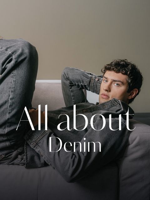 Ein junger Mann in einer grauen Jeansjacke und Jeans lehnt auf einem Sofa, über das Bild ist der Schriftzug „All about Denim“ gelegt.