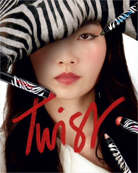 Eine Frau mit einem Hut mit Zebrastreifen und auffälligem Make-up ist von bunten Lippenstiften umgeben. Über das Bild zieht sich in roter Schrift das Wort „Twist“.