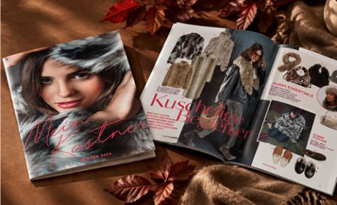 Ein Wintermodekatalog mit Kleidung und Accessoires, der auf einer mit Herbstblättern bedeckten Fläche aufgeschlagen liegt.