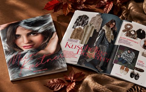 Ein Wintermodekatalog mit Kleidung und Accessoires, der auf einer mit Herbstblättern bedeckten Fläche aufgeschlagen liegt.
