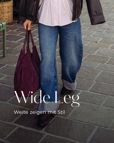 Eine Person, die eine Jacke, ein plissiertes Hemd und eine weit geschnittene Jeans mit Umschlag trägt, hält eine große, dunkelviolette Tragetasche in der Hand. Der Text darüber lautet: „Wide Leg. Weite zeigen mit Stil.“.