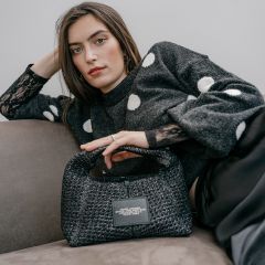 Eine Frau in einem grauen Pullover mit Polka-Dots, die eine strukturierte Marc-Jacobs-Handtasche in der Hand hält.