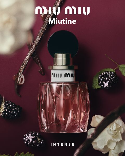 Ein rosa Parfümflakon mit der Aufschrift „Miu Miu Miutine“ auf burgunderrotem Hintergrund, umgeben von Beeren, Vanilleschoten und weißen Blüten.